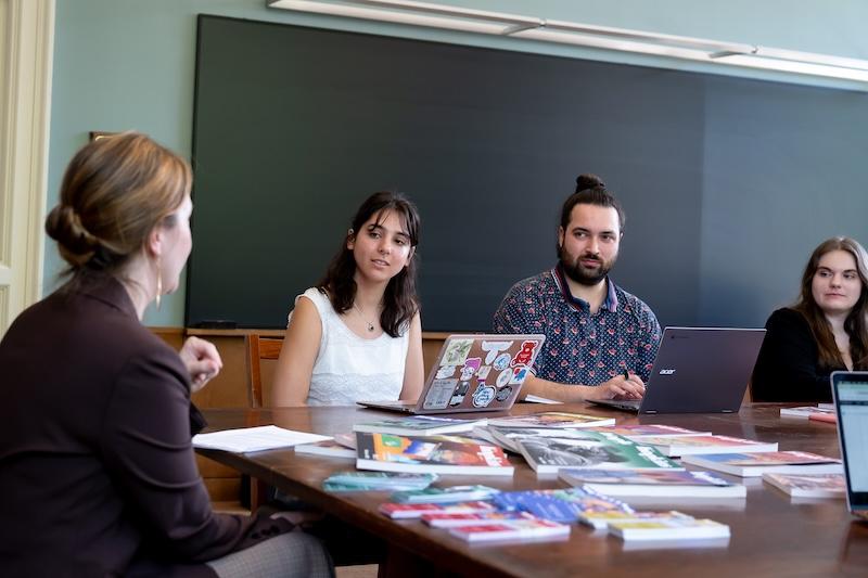 Four people sit around a table with open laptops and many copies of a lit magazine